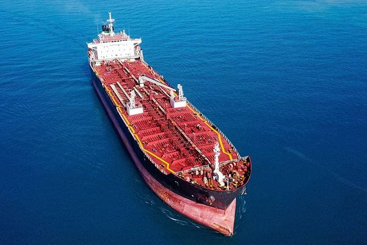 Large oil tanker with red deck and white superstructure cruising through calm blue ocean waters.