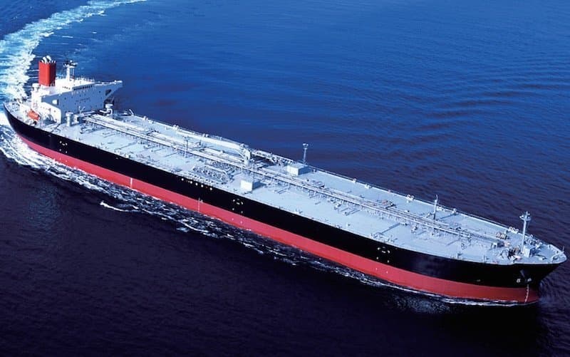 Massive oil tanker with a black and red hull cruising through deep blue ocean waters.